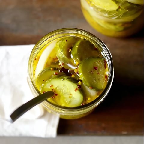 A jar of pickles with a spoon in it.
