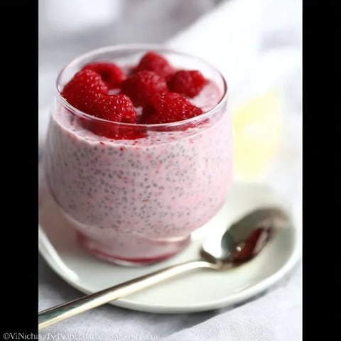 A bowl of raspberry yogurt with a spoon in it.