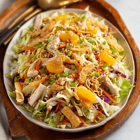 A plate of chicken salad with lettuce, carrots, and oranges.
