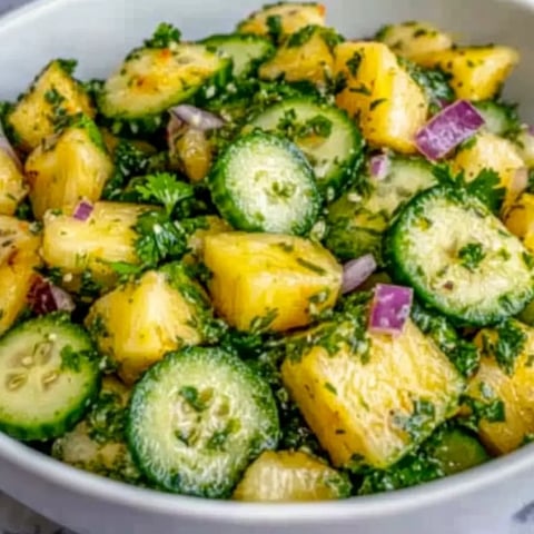 A bowl of vegetables including cucumbers, onions, and pineapple.